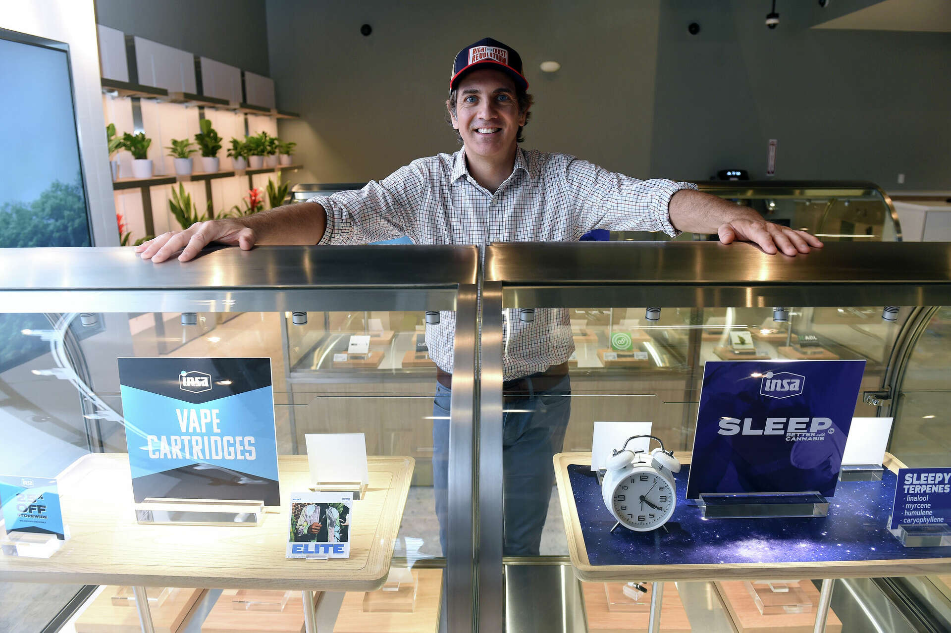 A dispensary manager standing behind a counter showcasing vape cartridges and sleep products in a modern cannabis dispensary.